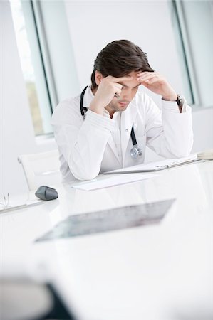 Male doctor sitting in his office and looking upset Stock Photo - Premium Royalty-Free, Code: 6108-05867999