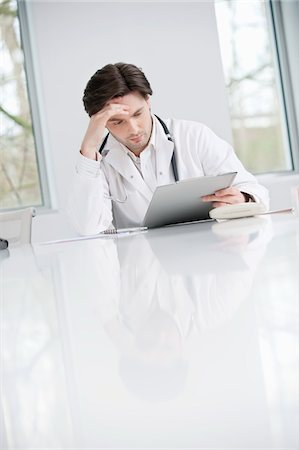 Male doctor examining a medical report and looking upset Stock Photo - Premium Royalty-Free, Code: 6108-05868003