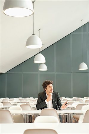 Businessman sitting at a cafeteria and talking on a mobile phone Stock Photo - Premium Royalty-Free, Code: 6108-05868391