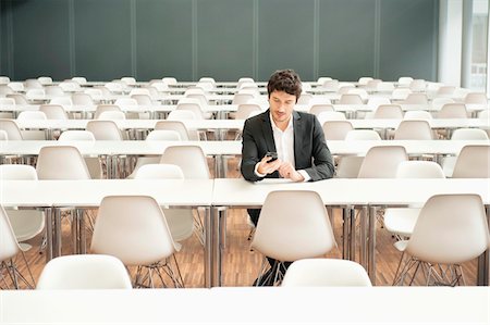 Businessman sitting at a cafeteria and using a mobile phone Stock Photo - Premium Royalty-Free, Code: 6108-05868405