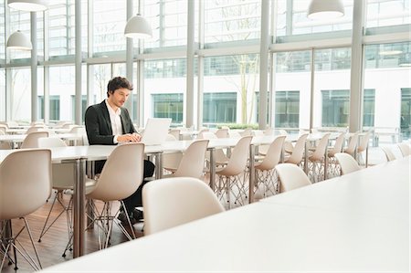 Businessman sitting at a cafeteria and using a laptop Stock Photo - Premium Royalty-Free, Code: 6108-05868410
