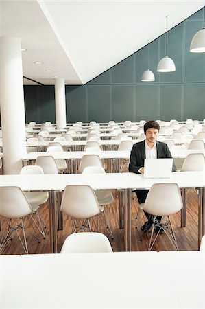 Businessman sitting at a cafeteria and using a laptop Stock Photo - Premium Royalty-Free, Code: 6108-05868416