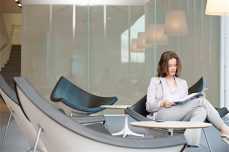 Businesswoman sitting on a chair and reading a magazine Stock Photo - Premium Royalty-Free, Code: 6108-05868808