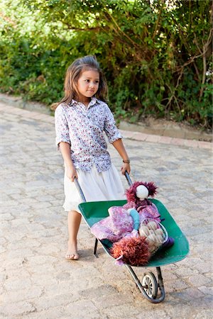 Cute girl pushing a wheelbarrow filled with toys Foto de stock - Sin royalties Premium, Código: 6108-05869488