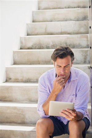 Mid adult man sitting on steps and using a digital tablet Stock Photo - Premium Royalty-Free, Code: 6108-05869679