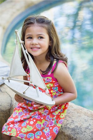 Little girl sitting by the swimming pool with model of boat in hand Stock Photo - Premium Royalty-Free, Code: 6108-05869698