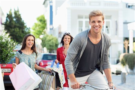 shopping friends caucasian - Young man cycling with two women standing in the background Stock Photo - Premium Royalty-Free, Code: 6108-05869611
