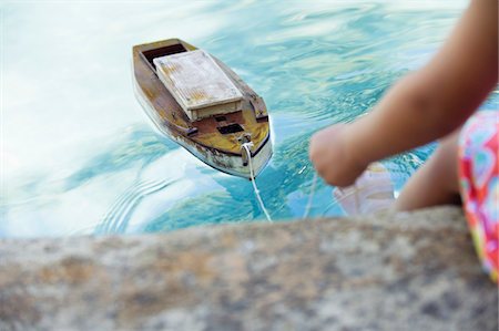 Low section view of a girl sitting at edge of swimming pool with toy boat in water Foto de stock - Sin royalties Premium, Código: 6108-05869717