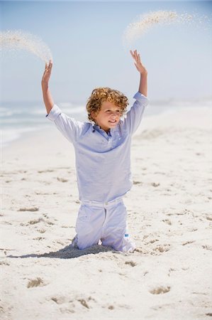 Garçon jouant dans le sable avec ses bras levés Photographie de stock - Premium Libres de Droits, Code: 6108-05869723