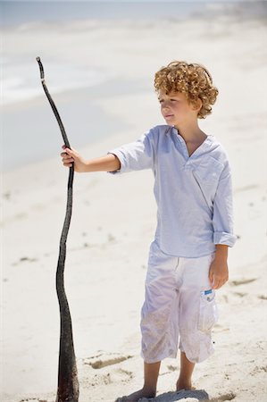 pre teen white beach - Boy holding a wooden stick on the beach Stock Photo - Premium Royalty-Free, Code: 6108-05869736