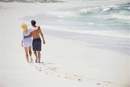 Rear view of a couple walking on the beach with their arms around each other Stock Photo - Premium Royalty-Free, Code: 6108-05869972