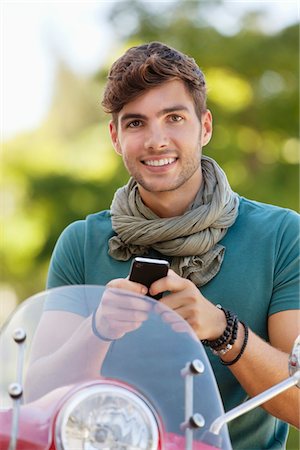 Portrait of a man sitting on a scooter and text messaging Stock Photo - Premium Royalty-Free, Code: 6108-05869929