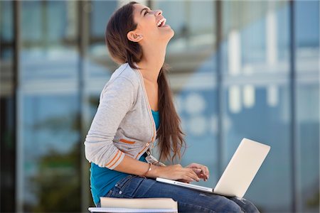 student with computer in campus - Woman laughing while using a laptop Stock Photo - Premium Royalty-Free, Code: 6108-05870070