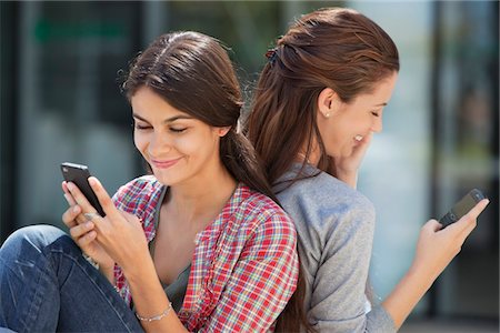 simsearch:6108-05870070,k - Two young women sitting back to back and text messaging Foto de stock - Sin royalties Premium, Código: 6108-05870093