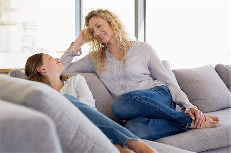 Mid adult woman and her daughter sitting on a couch and smiling Stock Photo - Premium Royalty-Free, Code: 6108-05870418