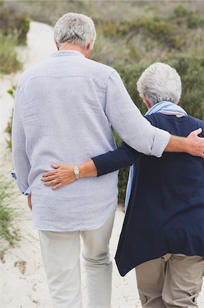 Rear view of a senior couple walking on the beach with their arms around each other Stock Photo - Premium Royalty-Free, Code: 6108-05870979