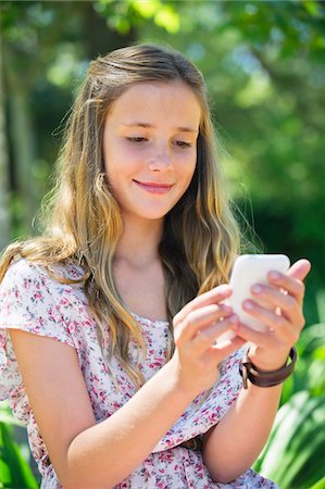 photo of pretty girl - Smiling little girl text messaging using a mobile phone Stock Photo - Premium Royalty-Free, Code: 6108-05871094