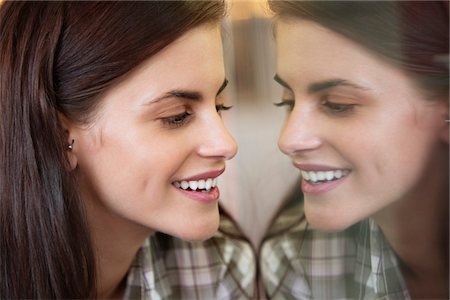 Smiling woman looking at her own reflection in the mirror Stock Photo - Premium Royalty-Free, Code: 6108-05871168