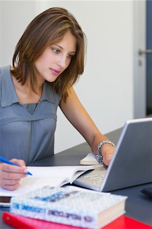 e-learning - Beautiful woman writing in book while using laptop in classroom Stock Photo - Premium Royalty-Free, Code: 6108-05871264