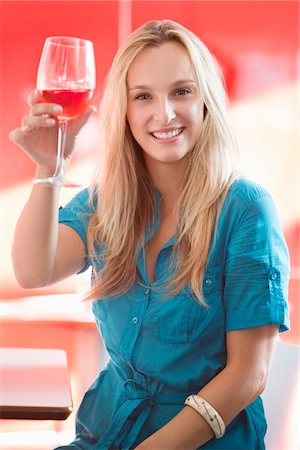Young woman toasting wine glass and smiling in a bar Stock Photo - Premium Royalty-Free, Code: 6108-05871480