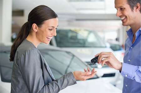 selling car - Happy salesperson handing car key to a woman in a showroom Stock Photo - Premium Royalty-Free, Code: 6108-05871401