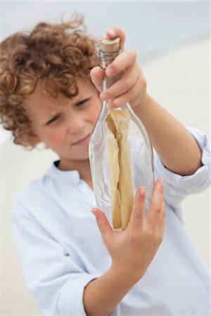 Boy looking at message in a bottle on beach Foto de stock - Royalty Free Premium, Número: 6108-05871548