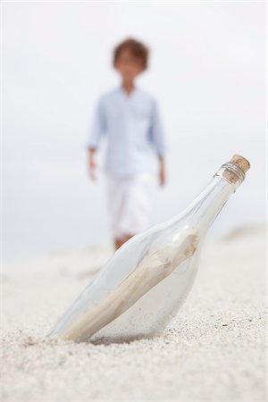Blurred boy walking towards bottle with note inside on beach Stock Photo - Premium Royalty-Free, Code: 6108-05871556
