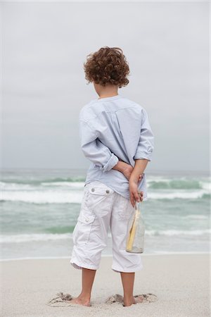 Vue arrière d'un garçon tenant la bouteille avec le message sur la plage Photographie de stock - Premium Libres de Droits, Code: 6108-05871569