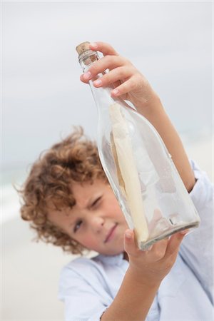 Boy looking at message in a bottle on beach Foto de stock - Sin royalties Premium, Código: 6108-05871585