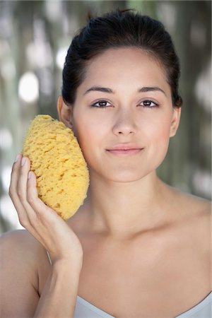 Beautiful young woman holding a bath sponge on her face Stock Photo - Premium Royalty-Free, Code: 6108-05871704