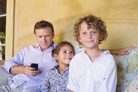 Portrait of a little boy with sister and father using a mobile phone while sitting on couch Stock Photo - Premium Royalty-Free, Code: 6108-05871937