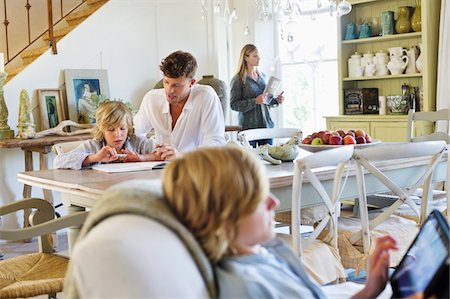 dad reads to children the book in the chair - Man teaching little boy while family members busy doing their work at house Stock Photo - Premium Royalty-Free, Code: 6108-05872034