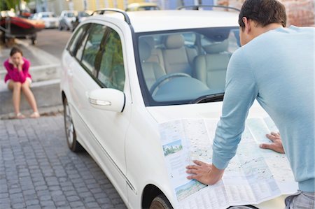 Rear view of a man looking at map on car with young woman sitting in the background Stock Photo - Premium Royalty-Free, Code: 6108-05872186