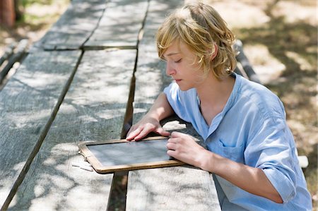 Side profile of a little boy writing on slate outdoors Stock Photo - Premium Royalty-Free, Code: 6108-05872683