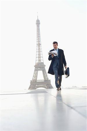 paris eiffel - Businessman walking with briefcase reading newspaper with the Eiffel Tower in the background, Paris, Ile-de-France, France Stock Photo - Premium Royalty-Free, Code: 6108-05872902