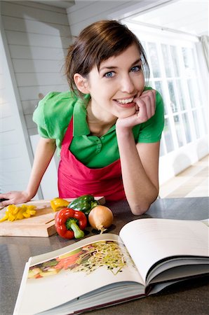Young woman looking at recipe book, vegetables on a chopping board Stock Photo - Premium Royalty-Free, Code: 6108-05873451