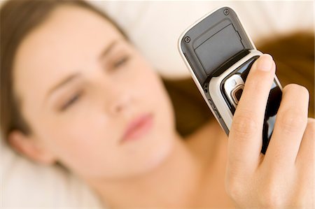 Portrait d'une jeune femme allongée sur un lit, tenant sa cellule Photographie de stock - Premium Libres de Droits, Code: 6108-05873533