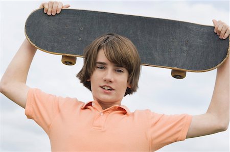 Portrait of a boy holding a skateboard over his head Stock Photo - Premium Royalty-Free, Code: 6108-05873681