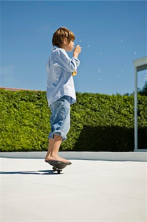 Boy blowing bubbles with a bubble wand while skateboarding Stock Photo - Premium Royalty-Free, Code: 6108-05874062