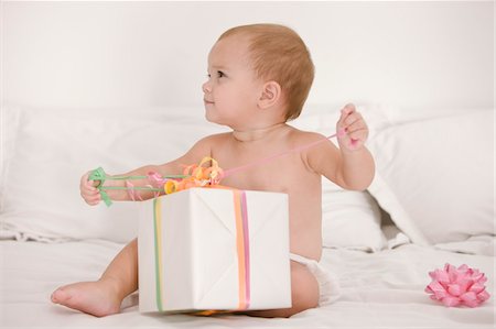 Baby girl playing with a present on the bed Stock Photo - Premium Royalty-Free, Code: 6108-05874010