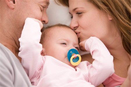 pacifier mom holding - Parents kissing their daughter Stock Photo - Premium Royalty-Free, Code: 6108-05874032