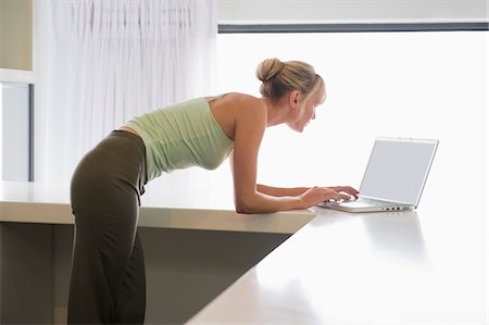 simsearch:6108-05859712,k - Woman leaning on a counter and working on a laptop Foto de stock - Royalty Free Premium, Número: 6108-05874487