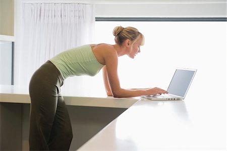 simsearch:6108-05859712,k - Woman leaning on a counter and working on a laptop Foto de stock - Royalty Free Premium, Número: 6108-05874488