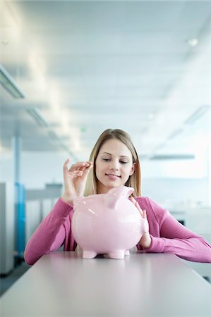 Businesswoman inserting a coin into a piggy bank Stock Photo - Premium Royalty-Free, Code: 6108-05874788