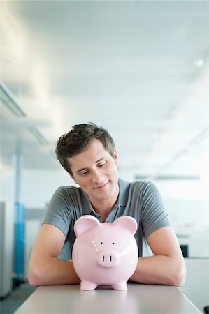 Businessman looking at a piggy bank and smiling Stock Photo - Premium Royalty-Free, Code: 6108-05874790