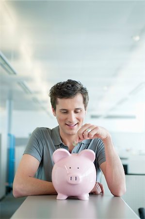 Businessman inserting a coin into a piggy bank Stock Photo - Premium Royalty-Free, Code: 6108-05874792