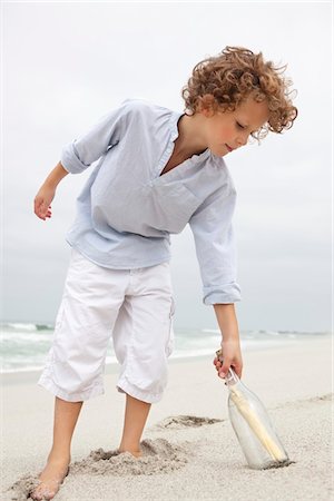 rolled up sleeves - Boy reaching for message in a bottle on beach Stock Photo - Premium Royalty-Free, Code: 6108-05874977