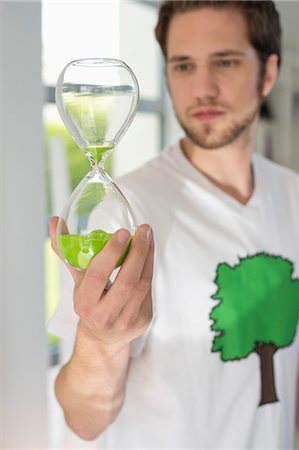 Man looking at an hourglass with green sand in it Stock Photo - Premium Royalty-Free, Code: 6108-06165990