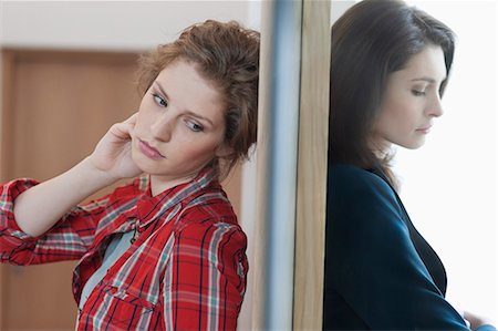 Two female friends standing back to back against a door Stock Photo - Premium Royalty-Free, Code: 6108-06166369