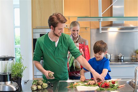 Parents looking at their son cutting vegetables in the kitchen Foto de stock - Sin royalties Premium, Código: 6108-06166784